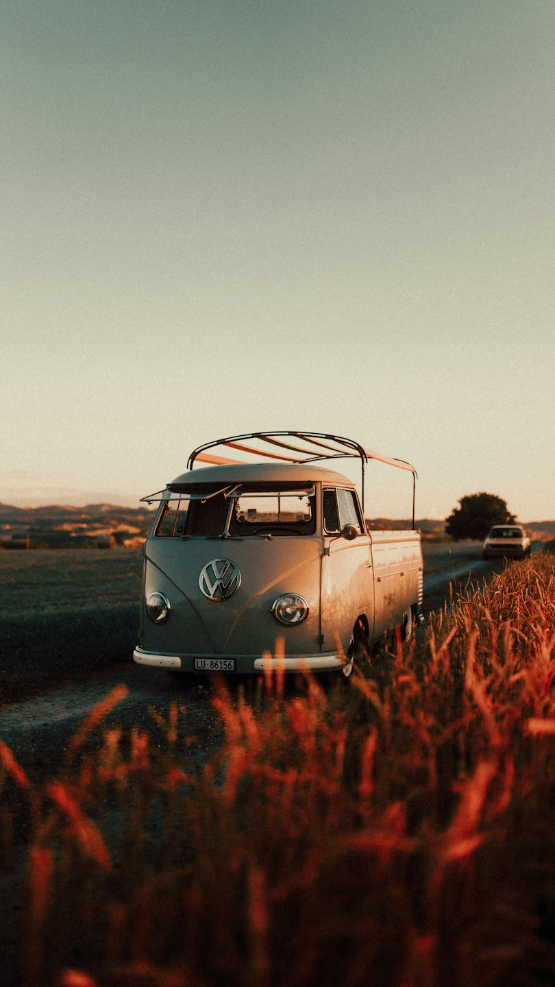 Starý Volkswagen autobus zaparkovaný na poľnej ceste v zlatom svetle.
